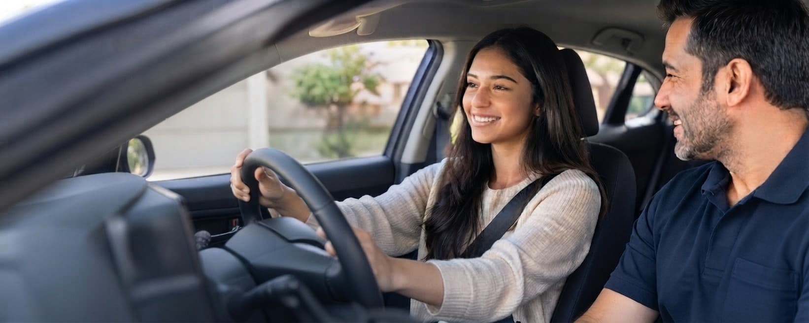 A learner driver at the wheel, smiling alongside her instructor